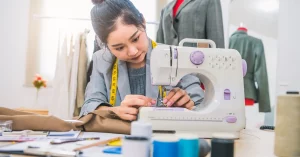 Fashion designer focused on sewing fabric with a machine in a design studio.